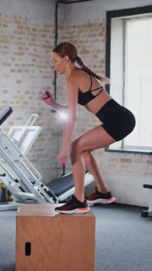 Dikey. Fitness meraklısı engelin üzerinden atlıyor. Spor salonu: engellerin üzerinden atlayan kadın. Fitness meraklısı spor salonunda vücut egzersizi yapıyor. mekik çekerken karın kaslarına odaklanan bir kadın. Sahneye çıkan kadın