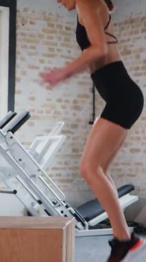 Dikey. Fitness meraklısı engelin üzerinden atlıyor. Spor salonu: engellerin üzerinden atlayan kadın. Fitness meraklısı spor salonunda vücut egzersizi yapıyor. mekik çekerken karın kaslarına odaklanan bir kadın. Sahneye çıkan kadın