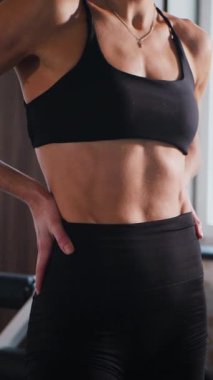 Dikey. Atletik giyinmiş genç bir kadın parlak bir spor salonunda dikiliyor. Spor salonunda kararlı görünen bir kadın. Spor salonundaki antrenmana ara veren zinde bir kadın. Gülümsüyor