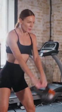 Dikey. Kettlebell 'i kararlılıkla kaldıran kadın. Kettlebell 'le spor yapıyorum. Güç eğitimi iş başında. Kettlebell kaldırma ile fitness odağı. Kadın spor salonunda çekirdek egzersizi yapıyor. Fitness meraklısı