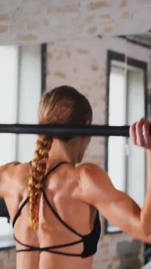 Dikey. Spor salonunda halterle çömelmiş bir kadın. Spor meraklısı ağırlıklarla çömelme hareketi yapıyor. Güçlü kadın antrenmanda halter kaldırıyor. Spor salonunda halterle egzersiz yapan bir kadın. Kadın spor salonunda vücut egzersizi yapıyor.