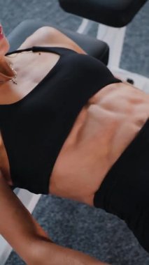 Dikey. Spor kıyafetli bir kadın egzersiz minderinde mekik çekiyor. Koltuk değnekli karın kasları üzerinde çalışan bir bayan sporcu. Fitness meraklısı spor salonunda vücut egzersizi yapıyor. mekik çekerken karın kaslarına odaklanan kadın..