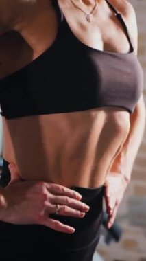 Dikey. Atletik giyinmiş genç bir kadın parlak bir spor salonunda dikiliyor. Spor salonunda kararlı görünen bir kadın. Spor salonundaki antrenmana ara veren zinde bir kadın. Gülümsüyor