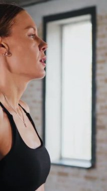 Dikey. Atletik giyinmiş genç bir kadın parlak bir spor salonunda dikiliyor. Spor salonunda kararlı görünen bir kadın. Spor salonundaki antrenmana ara veren zinde bir kadın. Gülümsüyor