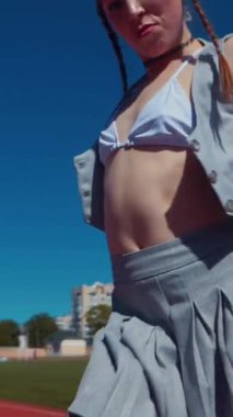 Dikey. Stadyum pistinde neşeyle dans eden iki ateşli kadın. Kısa etekli ponpon kızlar koşu pistinde mutlu bir şekilde dans ediyorlar. İki kız spor pistinde baştan çıkarıcı bir şekilde dans ediyor.