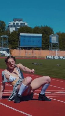 Dikey. Stadyum pistinde neşeyle dans eden iki ateşli kadın. Kısa etekli ponpon kızlar koşu pistinde mutlu bir şekilde dans ediyorlar. İki kız spor pistinde baştan çıkarıcı bir şekilde dans ediyor.