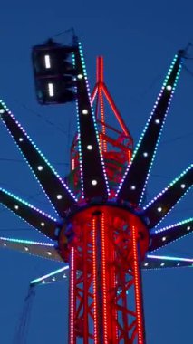 Dikey. Gece gökyüzüne karşı parlayan ışıklarla süslenmiş canlı bir eğlence gezisi. Luna Parkı. Parlak yeşil ışıklar lunaparktaki dönen bir atlıkarıncanın üzerinde dans ediyor. Ekstrem atlıkarınca neşeyle dönüyor, büyüleyici yeşil ışıklarla aydınlatılıyor