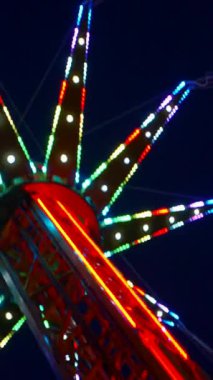 Dikey. Gece gökyüzüne karşı parlayan ışıklarla süslenmiş canlı bir eğlence gezisi. Luna Parkı. Parlak yeşil ışıklar lunaparktaki dönen bir atlıkarıncanın üzerinde dans ediyor. Ekstrem atlıkarınca neşeyle dönüyor, büyüleyici yeşil ışıklarla aydınlatılıyor