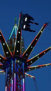 Dikey. Gece gökyüzüne karşı parlayan ışıklarla süslenmiş canlı bir eğlence gezisi. Luna Parkı. Parlak yeşil ışıklar lunaparktaki dönen bir atlıkarıncanın üzerinde dans ediyor. Ekstrem atlıkarınca neşeyle dönüyor, büyüleyici yeşil ışıklarla aydınlatılıyor
