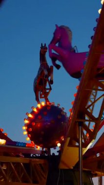 Dikey. Gece gökyüzüne karşı parlayan ışıklarla süslenmiş canlı bir eğlence gezisi. Luna Parkı. Parlak yeşil ışıklar lunaparktaki dönen bir atlıkarıncanın üzerinde dans ediyor. Ekstrem atlıkarınca neşeyle dönüyor, büyüleyici yeşil ışıklarla aydınlatılıyor