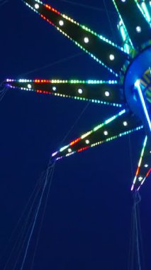 Dikey. Gece gökyüzüne karşı parlayan ışıklarla süslenmiş canlı bir eğlence gezisi. Luna Parkı. Parlak yeşil ışıklar lunaparktaki dönen bir atlıkarıncanın üzerinde dans ediyor. Ekstrem atlıkarınca neşeyle dönüyor, büyüleyici yeşil ışıklarla aydınlatılıyor