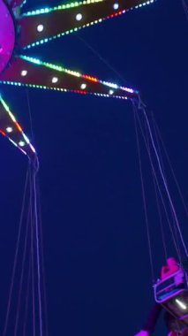 Dikey. Gece gökyüzüne karşı parlayan ışıklarla süslenmiş canlı bir eğlence gezisi. Luna Parkı. Parlak yeşil ışıklar lunaparktaki dönen bir atlıkarıncanın üzerinde dans ediyor. Ekstrem atlıkarınca neşeyle dönüyor, büyüleyici yeşil ışıklarla aydınlatılıyor
