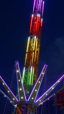 Dikey. Gece gökyüzüne karşı parlayan ışıklarla süslenmiş canlı bir eğlence gezisi. Luna Parkı. Parlak yeşil ışıklar lunaparktaki dönen bir atlıkarıncanın üzerinde dans ediyor. Ekstrem atlıkarınca neşeyle dönüyor, büyüleyici yeşil ışıklarla aydınlatılıyor