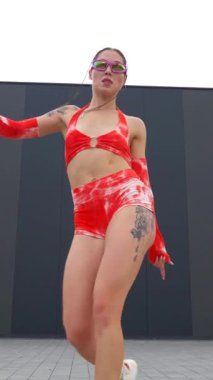 Dikey. Sokakta kırmızı mayo giymiş bir kız dans ediyor. Erotik dans eden kadın. Genç kız enerjik bir şekilde seksi bir dans ediyor. Çıplak kalçalarla dans eden bir kız..