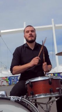 Dikey. Bir adam açık havada davul çalıyor. Güneşli bir günde bir grup dışarıda canlı çalar. Grup doğada çalıyor. Basçı, gitarist, davulcu, profesyonel, konser. Güzel manzara.