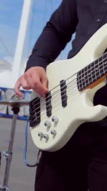 Dikey. Adam havalı bas gitar çalıyor. Stadyumun arka planında müzik grubu çalıyor. Profesyonel müzisyen. Meydanda şehir merkezinde bir müzik grubu çalıyor. Profesyonel müzisyen..
