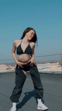 Dikey. Baştan çıkarıcı dans eden seksi kadın. Kıvranıyor. Siyah kıyafetler, berrak bir gökyüzü arkaplanı ve çatı dansı. Güneşte bir kıvılcım. Çatı performansı, büyüleyici bir vücut hareketi ve tarz gösterisi. Büyüleyici bir twerk gösterisi güçlü