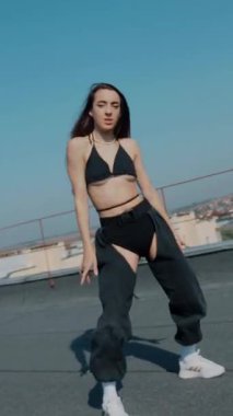 Dikey. Baştan çıkarıcı dans eden seksi kadın. Kıvranıyor. Siyah kıyafetler, berrak bir gökyüzü arkaplanı ve çatı dansı. Güneşte bir kıvılcım. Çatı performansı, büyüleyici bir vücut hareketi ve tarz gösterisi. Büyüleyici bir twerk gösterisi güçlü