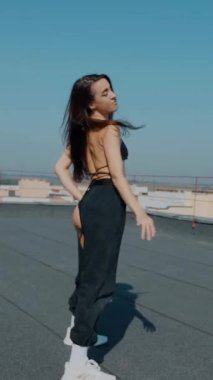 Dikey. Baştan çıkarıcı dans eden seksi kadın. Kıvranıyor. Siyah kıyafetler, berrak bir gökyüzü arkaplanı ve çatı dansı. Güneşte bir kıvılcım. Çatı performansı, büyüleyici bir vücut hareketi ve tarz gösterisi. Büyüleyici bir twerk gösterisi güçlü