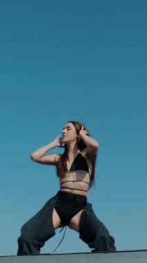 Dikey. Baştan çıkarıcı dans eden seksi kadın. Kıvranıyor. Siyah kıyafetler, berrak bir gökyüzü arkaplanı ve çatı dansı. Güneşte bir kıvılcım. Çatı performansı, büyüleyici bir vücut hareketi ve tarz gösterisi. Büyüleyici bir twerk gösterisi güçlü