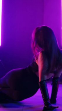 Dikey. Siyah elbiseli, neon ışıklı, baştan çıkarıcı dans performansı. Yüksek topuklu. Güzel kız erotik olarak kameraya poz veriyor. Parlak neon ışıklı dans pisti