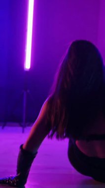 Dikey. Siyah elbiseli, neon ışıklı, baştan çıkarıcı dans performansı. Yüksek topuklu. Güzel kız erotik olarak kameraya poz veriyor. Parlak neon ışıklı dans pisti