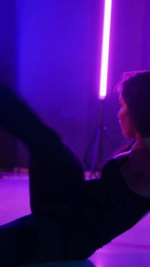 Dikey. Siyah elbiseli, neon ışıklı, baştan çıkarıcı dans performansı. Yüksek topuklu. Güzel kız erotik olarak kameraya poz veriyor. Parlak neon ışıklı dans pisti