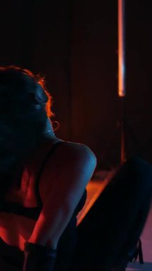 Dikey. Siyah elbiseli, neon ışıklı, baştan çıkarıcı dans performansı. Yüksek topuklu. Güzel kız erotik olarak kameraya poz veriyor. Parlak neon ışıklı dans pisti