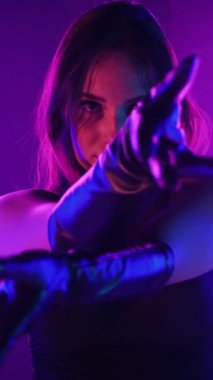 Dikey. Siyah elbiseli, neon ışıklı, baştan çıkarıcı dans performansı. Yüksek topuklu. Güzel kız erotik olarak kameraya poz veriyor. Parlak neon ışıklı dans pisti