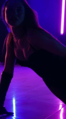 Dikey. Siyah elbiseli, neon ışıklı, baştan çıkarıcı dans performansı. Yüksek topuklu. Güzel kız erotik olarak kameraya poz veriyor. Parlak neon ışıklı dans pisti