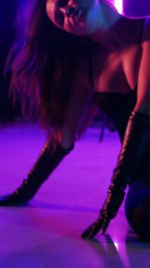 Dikey. Siyah elbiseli, neon ışıklı, baştan çıkarıcı dans performansı. Yüksek topuklu. Güzel kız erotik olarak kameraya poz veriyor. Parlak neon ışıklı dans pisti