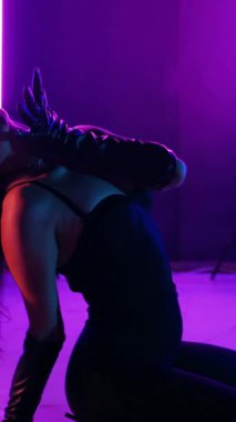 Dikey. Siyah elbiseli, neon ışıklı, baştan çıkarıcı dans performansı. Yüksek topuklu. Güzel kız erotik olarak kameraya poz veriyor. Parlak neon ışıklı dans pisti