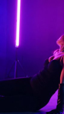 Dikey. Siyah elbiseli, neon ışıklı, baştan çıkarıcı dans performansı. Yüksek topuklu. Güzel kız erotik olarak kameraya poz veriyor. Parlak neon ışıklı dans pisti