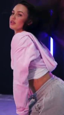 Dikey. Enerjik kız caz funk, hip hop, canlı neon fon ile dans ediyor. Genç kadın neon ışığı altında zarifçe hareket ediyor. Renkli neon ışıkların önünde dans eden kız. Neon ışıkları kızın neşesini aydınlatır.