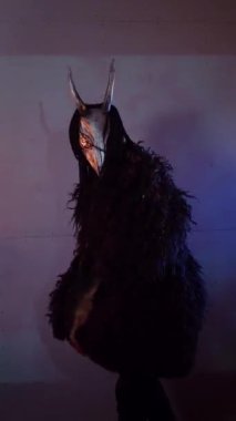 Dikey. Şeytan canavar elinde RGB çubuklarıyla dans ediyor. Korkunç maskeli mistik bir adam karanlık bir stüdyoda flüt çalar. Adam siyah bir ceket ve boynuzlu bir kafatası giymiş. Uzaylı uzaylı. Korkunç.,