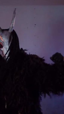 Dikey. Şeytan canavar elinde RGB çubuklarıyla dans ediyor. Korkunç maskeli mistik bir adam karanlık bir stüdyoda flüt çalar. Adam siyah bir ceket ve boynuzlu bir kafatası giymiş. Uzaylı uzaylı. Korkunç.,
