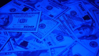 Canlı bir Amerikan para akışı var. Çok renkli ışıkta yıkanmış bir Amerikan doları yağmuru. ABD banknotlarının yakın plan görüntüsü. Detayları renkli bir renge bürünmüş. kağıt para döner.