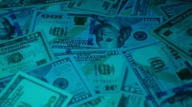 Canlı bir Amerikan para akışı var. Çok renkli ışıkta yıkanmış bir Amerikan doları yağmuru. ABD banknotlarının yakın plan görüntüsü. Detayları renkli bir renge bürünmüş. kağıt para döner.