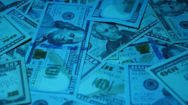 Canlı bir Amerikan para akışı var. Çok renkli ışıkta yıkanmış bir Amerikan doları yağmuru. ABD banknotlarının yakın plan görüntüsü. Detayları renkli bir renge bürünmüş. kağıt para döner.