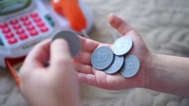 Oyun parasıyla dolu, satın almaya hazır bir çocuk eli. Oyuncak paralar, el ele yerleştirilmiş, sahte bir pazarı işaret ediyor. Oyun parasının tatmin edici tıkırtısı, bir çocuğun zevki. Minyatür bir pazar yeri, sahte işlemlerin yapıldığı yer..