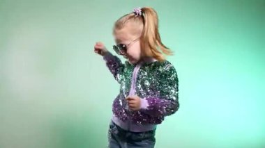 Stüdyoda renkli arka planda komik dans eden gülümseyen kız. Küçük hanım neşeyle gülüyor ve zevkle zıplıyor. Duygusal çocuk kameraya gülüyor. Disko partisi