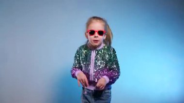 Stüdyoda renkli arka planda komik dans eden gülümseyen kız. Küçük hanım neşeyle gülüyor ve zevkle zıplıyor. Duygusal çocuk kameraya gülüyor. Disko partisi