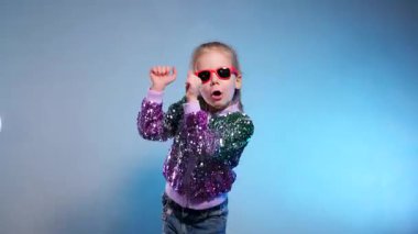 Stüdyoda renkli arka planda komik dans eden gülümseyen kız. Küçük hanım neşeyle gülüyor ve zevkle zıplıyor. Duygusal çocuk kameraya gülüyor. Disko partisi