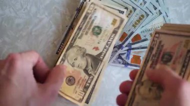 Bir yığın gevrek, dolar banknotları, becerikli ellerde tutuluyor. Adam kağıt para sayıyor. Bir Amerikan para akışı. Bir sürü Amerikan doları. ABD banknotlarının yakın plan görüntüsü. İşadamı elindeki banknotları sayar. Elinde parası olan adam..