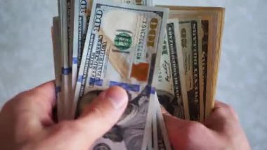 Bir yığın gevrek, dolar banknotları, becerikli ellerde tutuluyor. Adam kağıt para sayıyor. Bir Amerikan para akışı. Bir sürü Amerikan doları. ABD banknotlarının yakın plan görüntüsü. İşadamı elindeki banknotları sayar. Elinde parası olan adam..