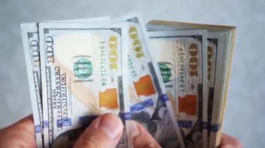 Bir yığın gevrek, dolar banknotları, becerikli ellerde tutuluyor. Adam kağıt para sayıyor. Bir Amerikan para akışı. Bir sürü Amerikan doları. ABD banknotlarının yakın plan görüntüsü. İşadamı elindeki banknotları sayar. Elinde parası olan adam..