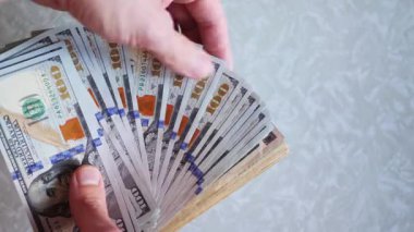 Bir yığın gevrek, dolar banknotları, becerikli ellerde tutuluyor. Adam kağıt para sayıyor. Bir Amerikan para akışı. Bir sürü Amerikan doları. ABD banknotlarının yakın plan görüntüsü. İşadamı elindeki banknotları sayar. Elinde parası olan adam..