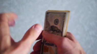 Bir yığın gevrek, dolar banknotları, becerikli ellerde tutuluyor. Adam kağıt para sayıyor. Bir Amerikan para akışı. Bir sürü Amerikan doları. ABD banknotlarının yakın plan görüntüsü. İşadamı elindeki banknotları sayar. Elinde parası olan adam..