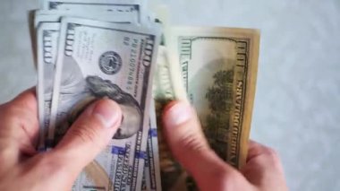 Bir yığın gevrek, dolar banknotları, becerikli ellerde tutuluyor. Adam kağıt para sayıyor. Bir Amerikan para akışı. Bir sürü Amerikan doları. ABD banknotlarının yakın plan görüntüsü. İşadamı elindeki banknotları sayar. Elinde parası olan adam..