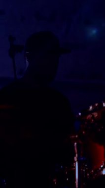 Dikey. Davulcu cool rock konserini çalar. Bir adam sahnede enerjik bir şekilde davul çalıyor arkasında parlak ışıklar yanıyor. Canlı performans sergileyen bir davulcu. Etrafı renkli sahne ışıklarıyla çevrili. Tutkuyla davul çalan bir adam 